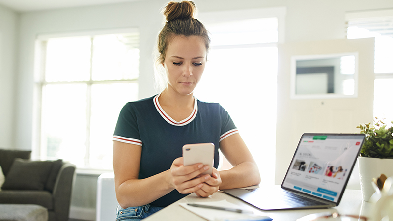 rapariga com telemóvel na mão numa secretária com computador
